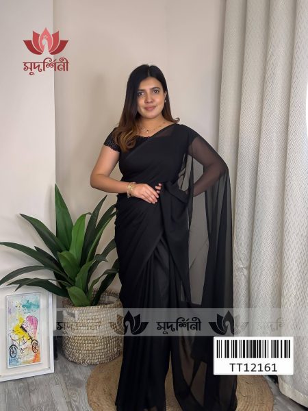 A woman wearing a black saree with a sheer sleeve poses indoors next to green plants and a curtain. Framed artwork sits on the floor. A logo and barcode are visible on the image.