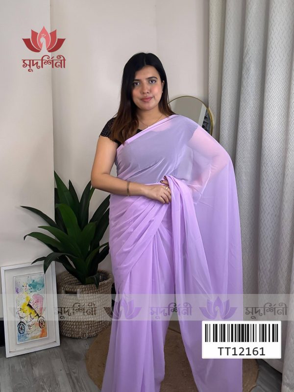A woman wearing a light purple saree with a black blouse stands indoors near a potted plant and a framed artwork. Light curtains and a mirror are in the background. The image includes a logo and a barcode. A woman wearing a light purple saree with a black blouse stands indoors near a potted plant and a framed artwork. Light curtains and a mirror are in the background. The image includes a logo and a barcode.