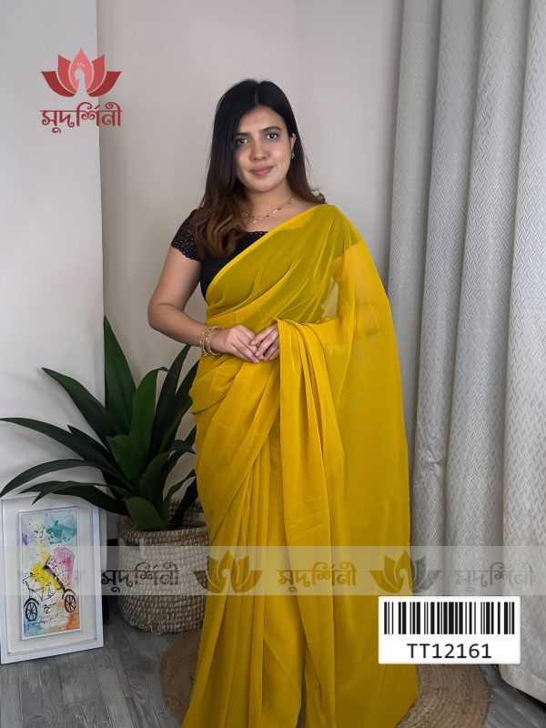 A woman wearing a bright yellow saree and black blouse stands indoors next to a potted plant and framed artwork, with a sheer curtain in the background. The logo “सुपर्निंदी” and a barcode are visible on the image. A woman wearing a bright yellow saree and black blouse stands indoors next to a potted plant and framed artwork, with a sheer curtain in the background. The logo “सुपर्निंदी” and a barcode are visible on the image.