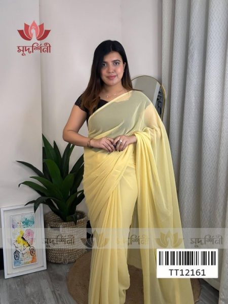 A woman stands indoors wearing a light yellow saree and a black blouse. She is smiling, with plants, a round mirror, and framed artwork in the background. A barcode and the code TT12161 are visible at the bottom of the image.